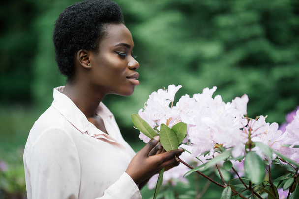 Портрет привлекательной афро-американской женщины, нюхающей цветок
 - Фото, изображение