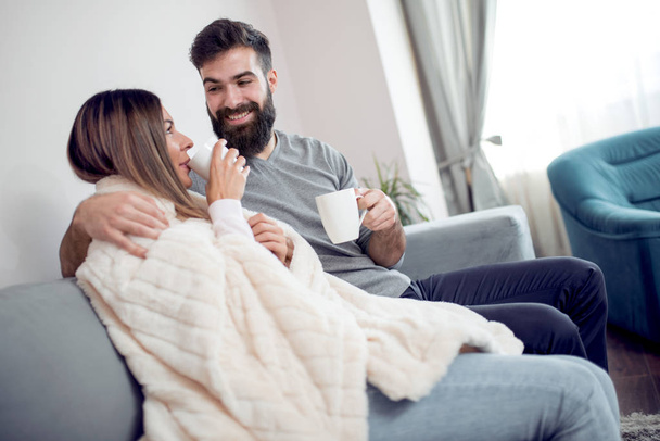 fröhliches romantisches Paar sitzt auf dem Sofa und lächelt. Sie trinken Tee. - Foto, Bild