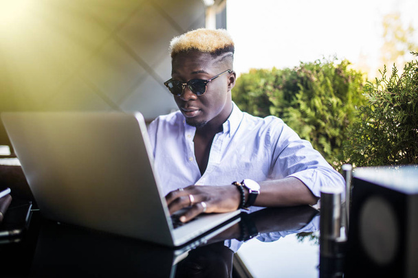アフリカ系アメリカ人の男性がカフェに座ってノートパソコンで作業している姿. - 写真・画像