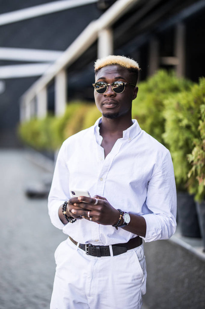 junger afroamerikanischer Mann steht in der Sommerstraße und tippt auf Handy - Foto, Bild