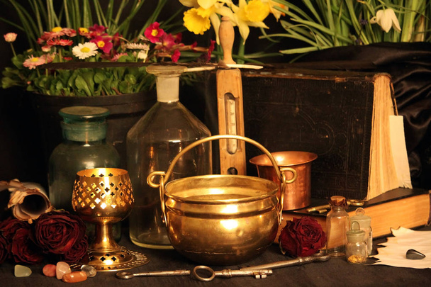 Black Magic Spells. Wiccan spells and herbs. Still Live: Old oil lamps, antique books, dried rose buds, a burning candle in a copper bowl, medicine bottles, lavender, Pulsatilla pratensis on an antique background. Wicca background. - Photo, Image