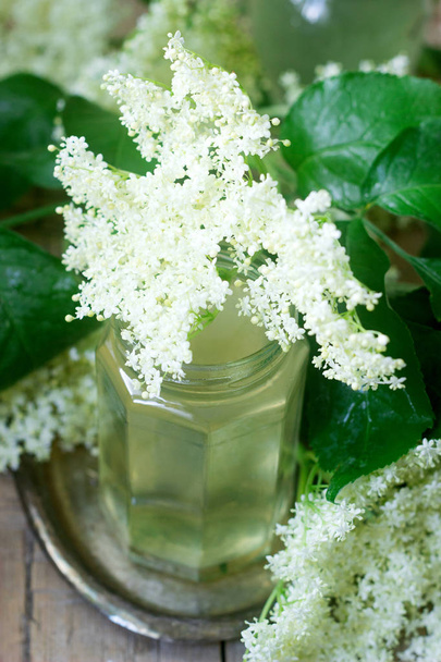 Homemade syrup of elderberry flowers in a glass jar and elder branches on a wooden table Rustic style, selective focus. - Φωτογραφία, εικόνα