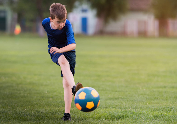Мальчик пинает футбол на спортивном поле во время футбольного матча
 - Фото, изображение