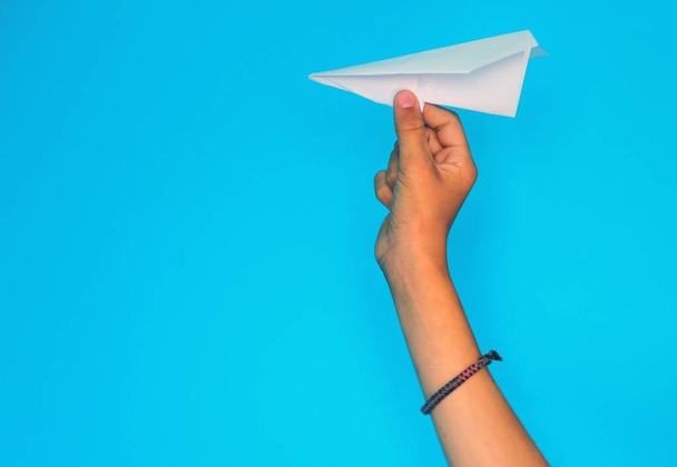 Children's hand throwing paper plane on blue background - Фото, изображение
