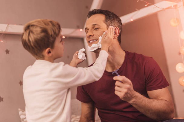 Delighted nice boy helping his father to shave - Foto, Imagen