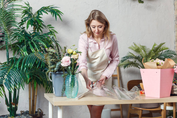 Photo of florist woman cutting film at table with flowers, paper - Foto, afbeelding