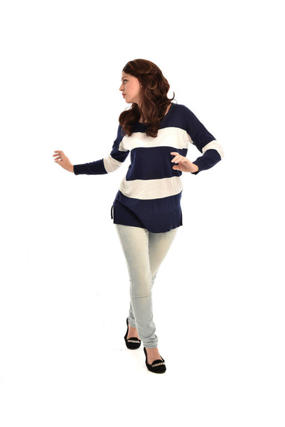 портрет дівчини в смугастому синьо-білому джемпері та джинсах. стояча поза на білому фоні студії
. - Фото, зображення