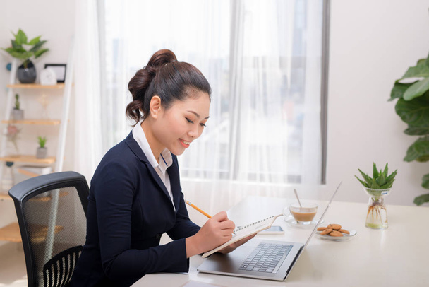 Mujer asiática freelancer manos femeninas con la escritura de la pluma en el cuaderno en casa u oficina
 - Foto, Imagen