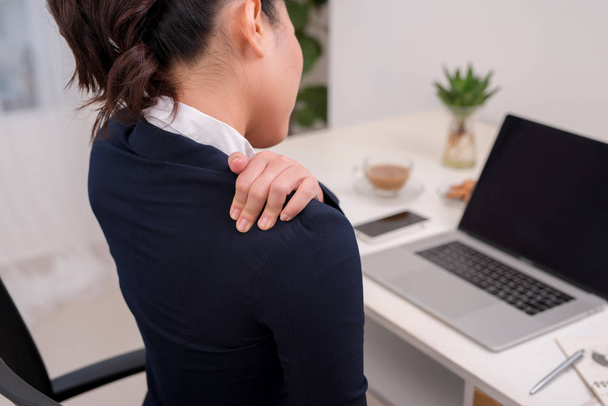 Young business person with neck pain. Focus on hand on neck with laptop on table in background. - Photo, Image