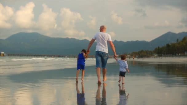 Young family, a father with his son and daughter, walks along the shore of the ocean, on the coast. A happy family walks along the seashore. - Кадри, відео