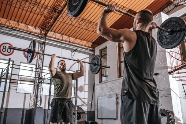 Two sportsmen lifting weights togethrt at gym. - Фото, изображение