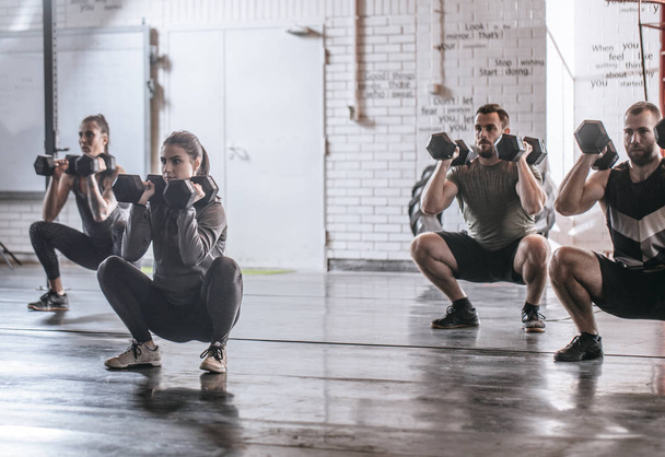 Group of sportsmen and sportswomen doing squats with weights at gym. - Fotoğraf, Görsel