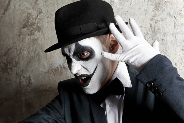 Scary evil clown wearing a bowler hat on wall background - Fotó, kép