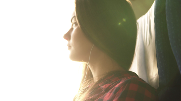 Low angle shooting. The young woman is going by train. The face is flooded with sun rays. Looks out the window, puts on the earphones. Long haired caucasian - Footage, Video