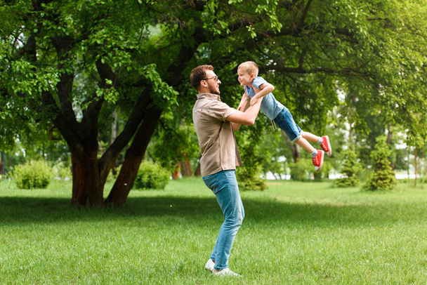 vista lateral do pai girando em torno do filho e eles se divertindo no parque
 - Foto, Imagem