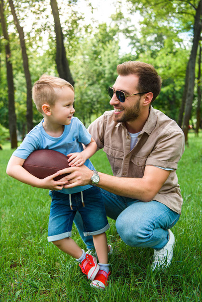 happy father and son with american football ball at park - Photo, Image