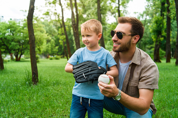 mosolyogva, átölelve apa-fiú baseball labda és kesztyű Park - Fotó, kép
