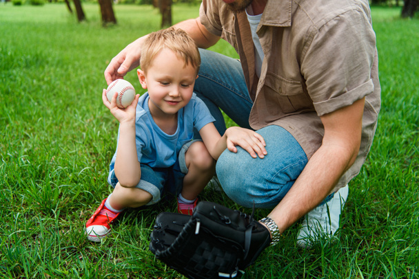 cropped image father and son with baseball ball and glove at park - Zdjęcie, obraz