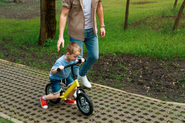 公園で自転車に乗って彼の息子を支える父のトリミングされた画像 - 写真・画像