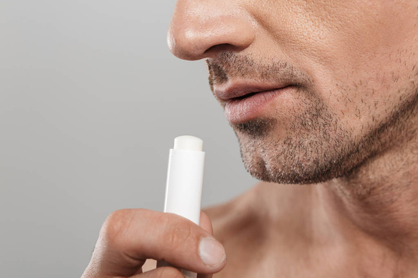 Cropped photo of of handsome mature man standing isolated over grey wall background naked holding lip balm. - Foto, Bild
