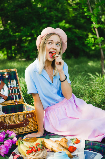 Portrait of happy young woman eating strawberries outdoors in park on picnic - Photo, image