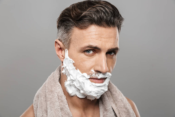 Photo of mature man standing isolated over grey wall background naked with shaving cream on face. - Foto, Bild