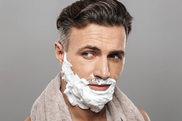 Photo of mature man standing isolated over grey wall background naked with shaving cream on face. - Zdjęcie, obraz