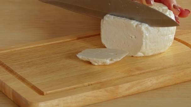 Woman is cutting Feta cheese with knife on wooden board. - Video