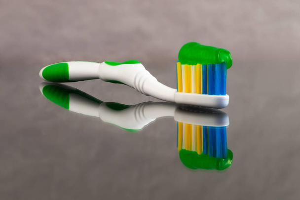 Un cepillo de dientes con una pasta de dientes con hierbas de color verde aplicado sobre él con una reflexión sobre un fondo abstracto gris con una gran profundidad de campo
. - Foto, Imagen