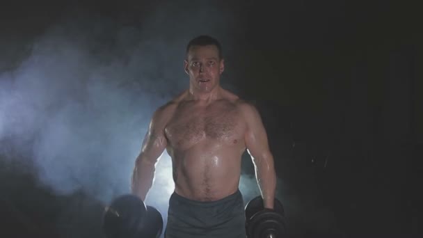 Strong sportsman lifting heavy dumbbells in smoke - 映像、動画