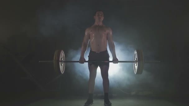 Strong sportsman lifting heavy dumbbells in smoke - Záběry, video