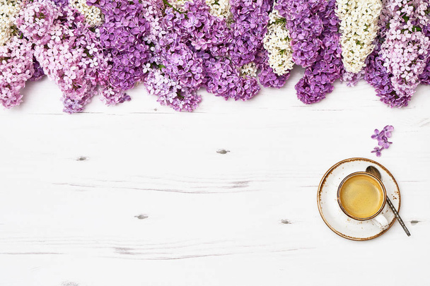 Taza de café y flores lila bordean sobre fondo de madera blanca. Espacio de copia, vista superior. Fondo de primavera
 - Foto, imagen