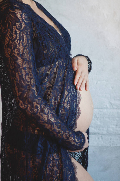 Zwangere vrouw in blauwe peignoir in haar buik knuffelen - Foto, afbeelding