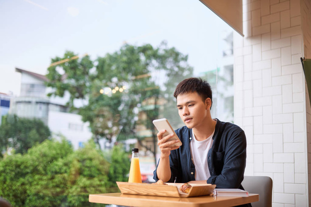 Miehet käyttävät älypuhelin istuu pöydässä kahvilassa
 - Valokuva, kuva