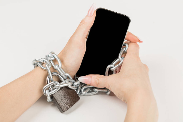 Železný řetěz se zámkem spojuje ženské ruky a smartphone dohromady. pojem závislost na mobilním telefonu. - Fotografie, Obrázek