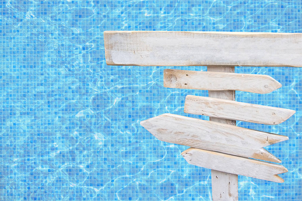 Белая деревенская деревянная стрелка знаки над бирюзовой голубой мозаики бассейн водной поверхности летом тема путешествия отдыха фон
.  - Фото, изображение