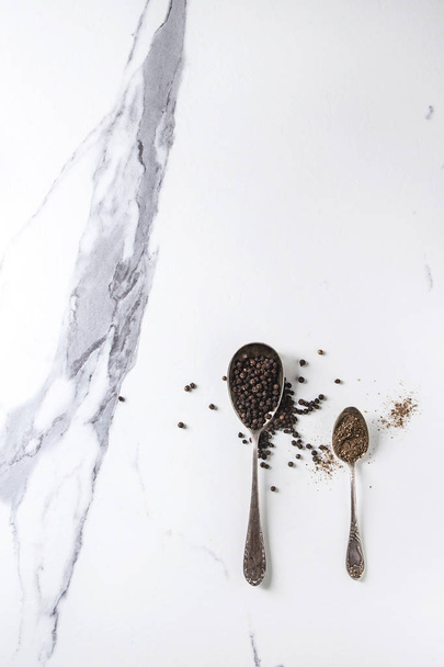 Black pepper peppercorns and ground powder in vintage spoons over white marble texture background. Top view, space. - Fotoğraf, Görsel