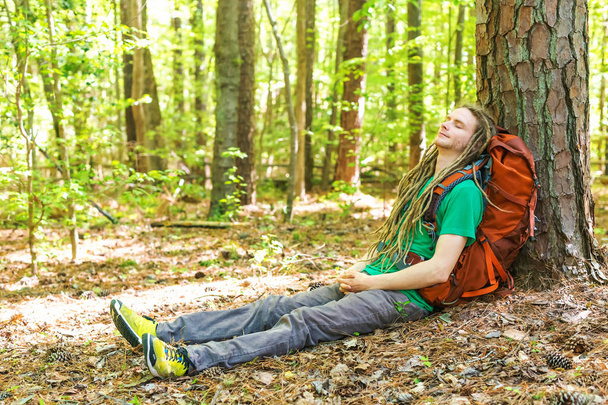 Hiker with backpack sleeping against a tree - Foto, afbeelding