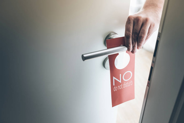 hand placing red do not disturb sign on handle of hotel room door - Photo, Image