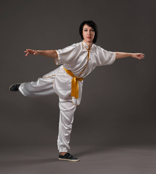 Young woman practicing tai chi chuan. Chinese management skill Qi's energy. Gray background, studio shoot. - Photo, Image