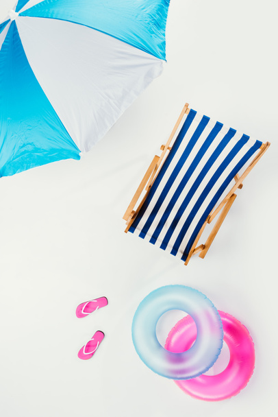 vista superior do guarda-chuva da praia, cadeira listrada da praia, chinelos e anéis infláveis isolados no branco
 - Foto, Imagem