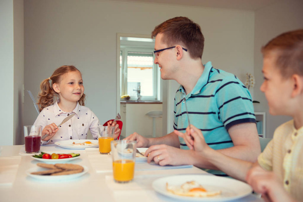 Happy father with his cute children talking at the breakfast at home - Fotoğraf, Görsel