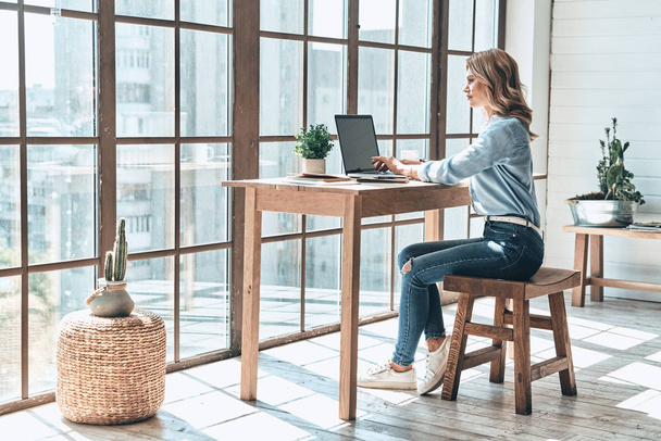 beautiful blonde woman using laptop at table while working in creative office at big window  - Zdjęcie, obraz