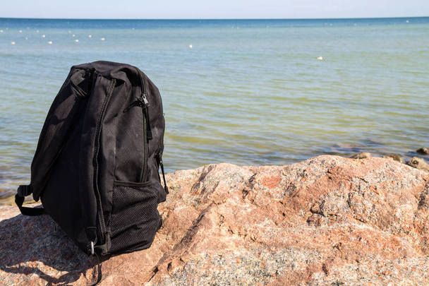 Tourist or traveler backpack on rock with sea shore background. Summer vacations concept - Photo, Image