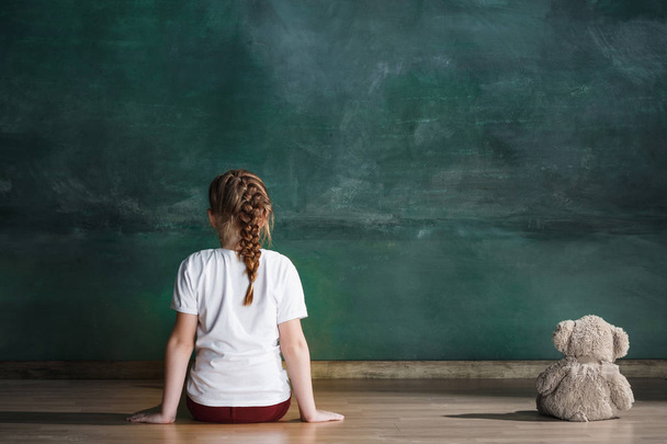 Little girl with teddy bear sitting on floor in empty room. Autism concept - Photo, image