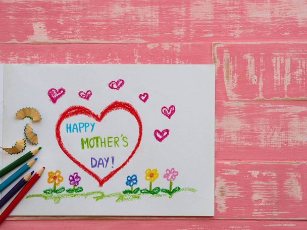 Il concetto della festa della mamma. Biglietto di auguri Happy Mothers Day disegnato da matite sulla carta su sfondo brillante texture di legno rosa
. - Foto, immagini
