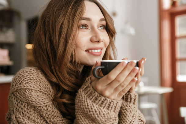 Portrait closeup of glad smiling woman with brown curly hair resting in cafe and drinking cup of tea or coffee - Фото, зображення