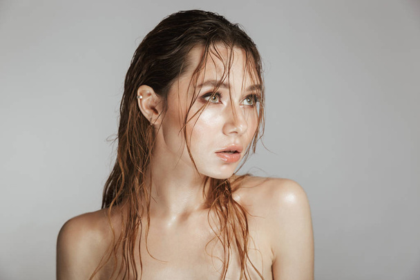 Fashion portrait of a topless beautiful woman with makeup and wet hair posing isolated over gray background - Photo, Image