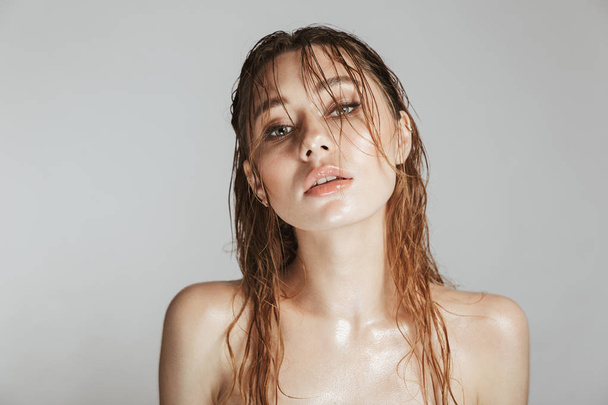 Fashion portrait of a topless young woman with makeup and wet hair posing isolated over gray background - Фото, изображение