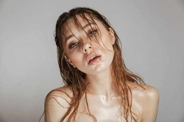 Fashion portrait of a topless young woman with makeup and wet hair posing isolated over gray background - Foto, Imagen